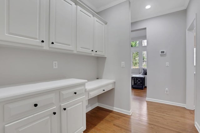 interior space with baseboards, crown molding, light wood-type flooring, built in desk, and recessed lighting