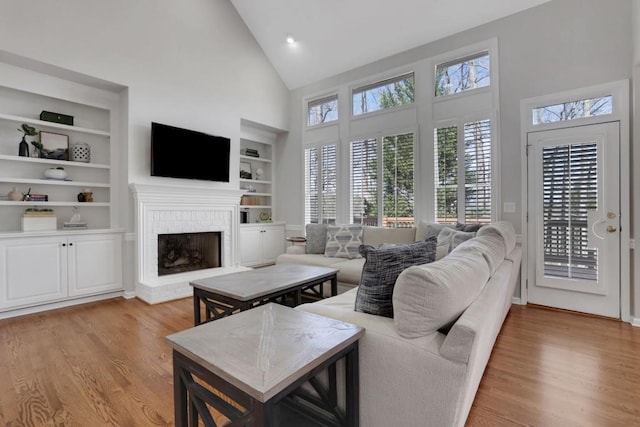 living room with built in shelves, a fireplace, a wealth of natural light, and light wood-style floors