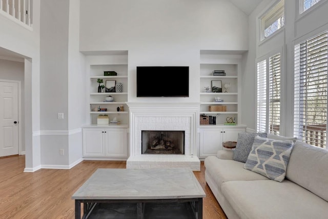 living room featuring high vaulted ceiling, light wood-style flooring, a fireplace, baseboards, and built in features