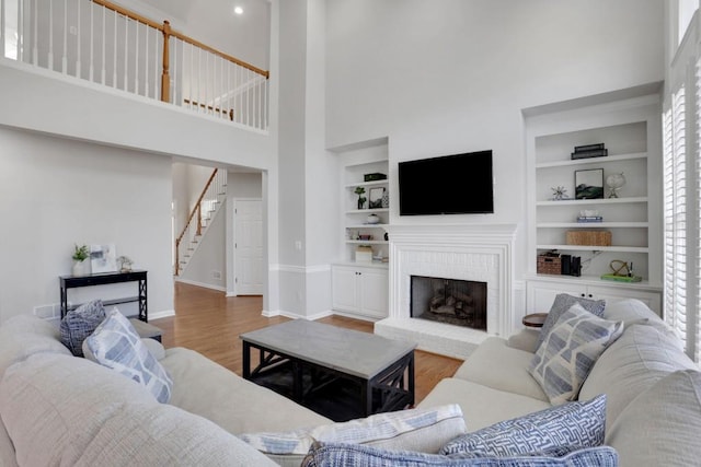 living area featuring baseboards, built in features, stairway, wood finished floors, and a brick fireplace