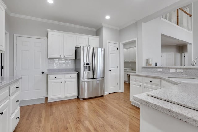 kitchen with crown molding, light wood-style flooring, white cabinets, a sink, and stainless steel fridge