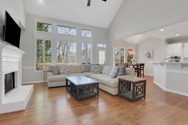 living area with ceiling fan, baseboards, a fireplace with raised hearth, and wood finished floors