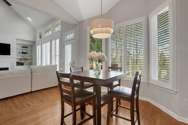 dining room featuring built in features, a fireplace, light wood-style floors, high vaulted ceiling, and baseboards