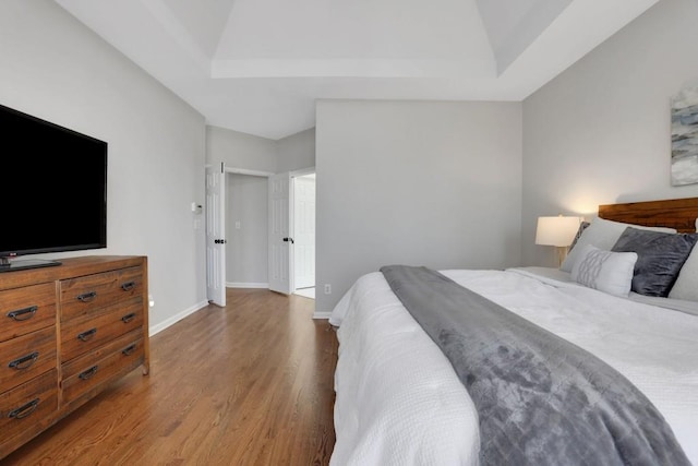 bedroom featuring a tray ceiling, baseboards, and wood finished floors