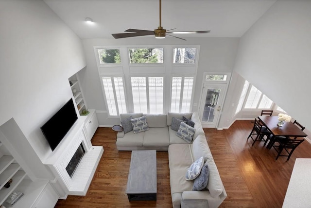 living room featuring dark wood-type flooring, a fireplace, a towering ceiling, and baseboards