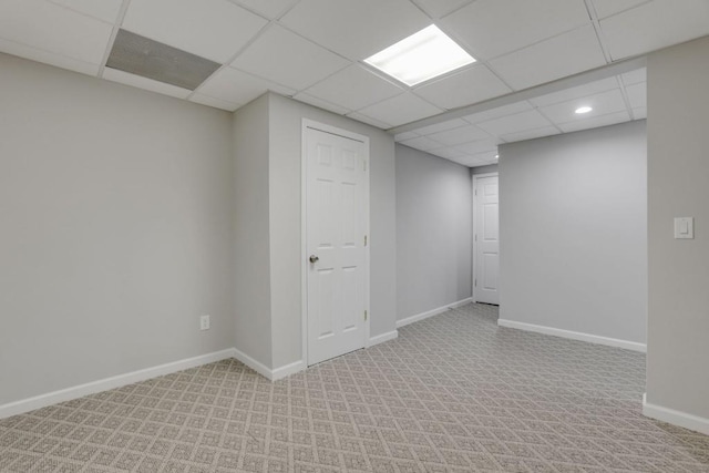 basement with a paneled ceiling, light colored carpet, and baseboards