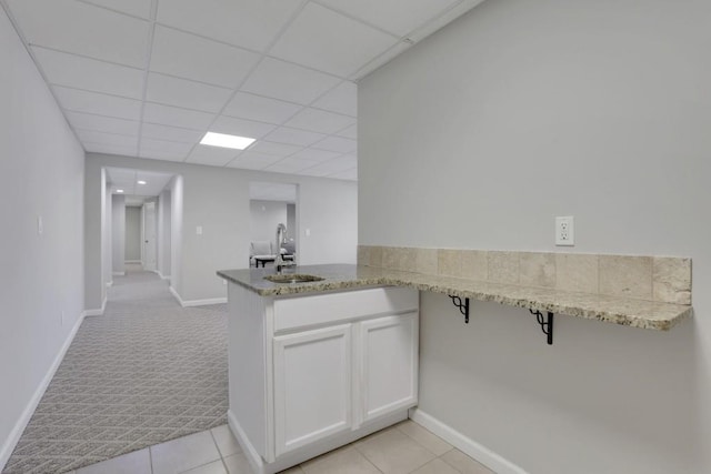 kitchen with white cabinets, light colored carpet, a peninsula, light stone countertops, and a sink