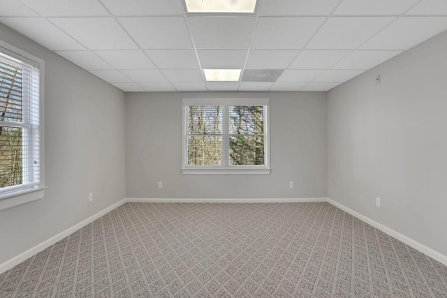 carpeted empty room featuring a paneled ceiling and baseboards