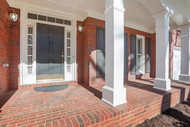 entrance to property featuring a porch and brick siding