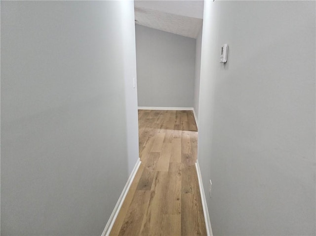 hallway with a textured ceiling, light wood-style flooring, and baseboards