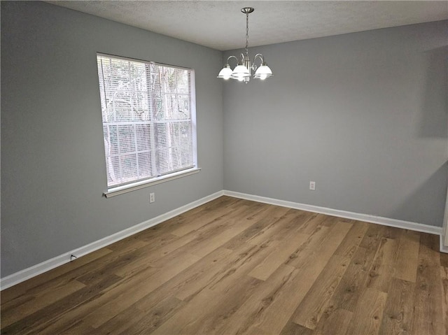 empty room featuring a chandelier, wood finished floors, and baseboards