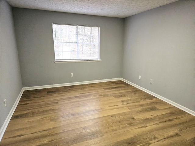 spare room with a textured ceiling, baseboards, and wood finished floors