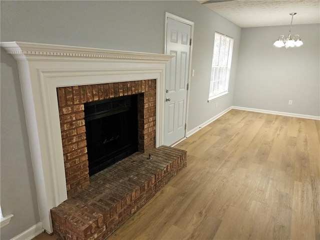 living room featuring light wood finished floors, a fireplace, an inviting chandelier, and baseboards