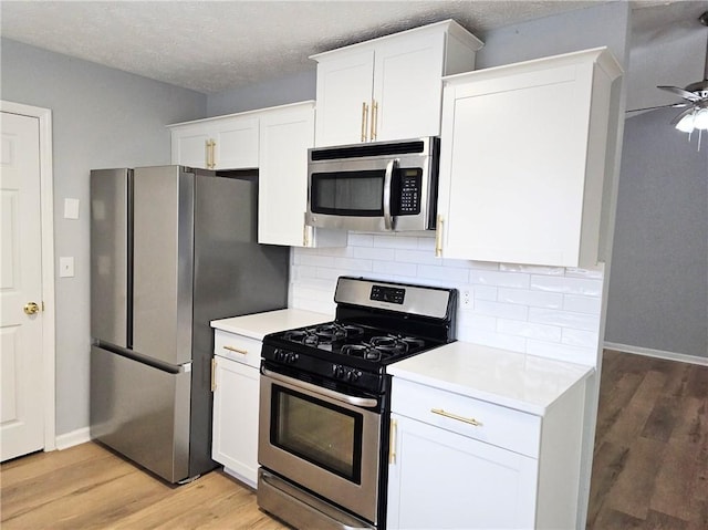 kitchen featuring light countertops, backsplash, appliances with stainless steel finishes, light wood-style floors, and white cabinetry