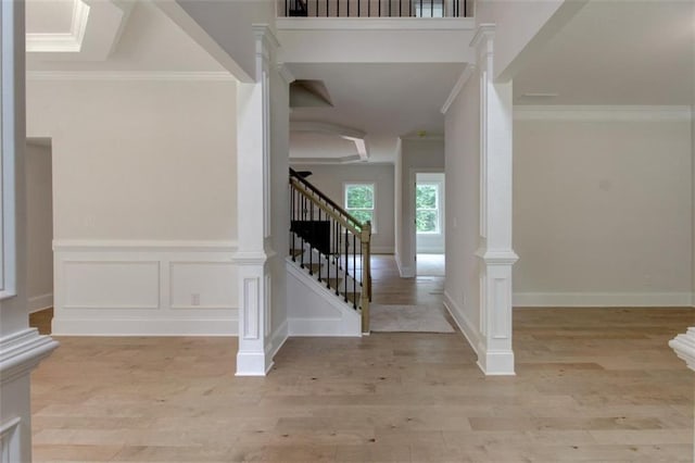 foyer featuring light wood-style floors, stairway, crown molding, ornate columns, and a decorative wall