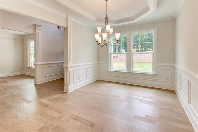 unfurnished dining area with light wood finished floors, a raised ceiling, a wealth of natural light, and an inviting chandelier