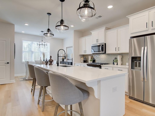 kitchen with visible vents, a center island with sink, a sink, tasteful backsplash, and stainless steel appliances