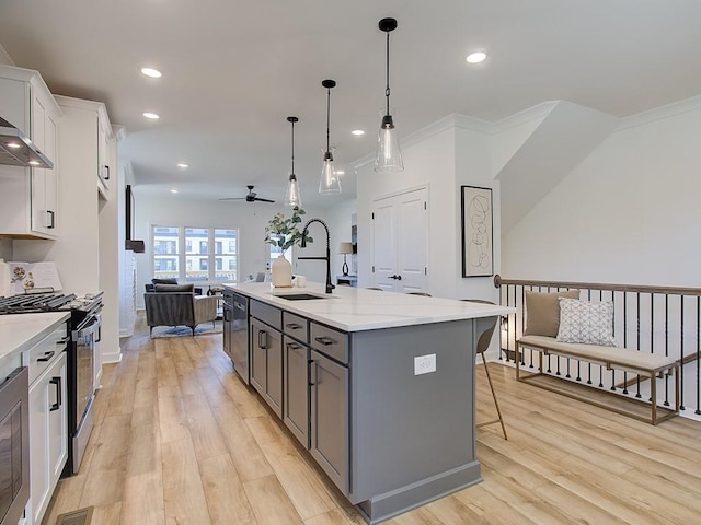 kitchen with appliances with stainless steel finishes, decorative light fixtures, white cabinetry, sink, and a center island with sink