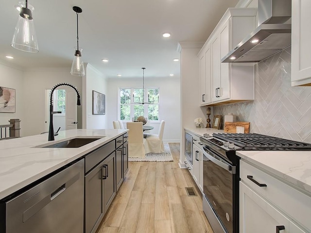 kitchen with appliances with stainless steel finishes, wall chimney exhaust hood, sink, white cabinets, and light stone counters