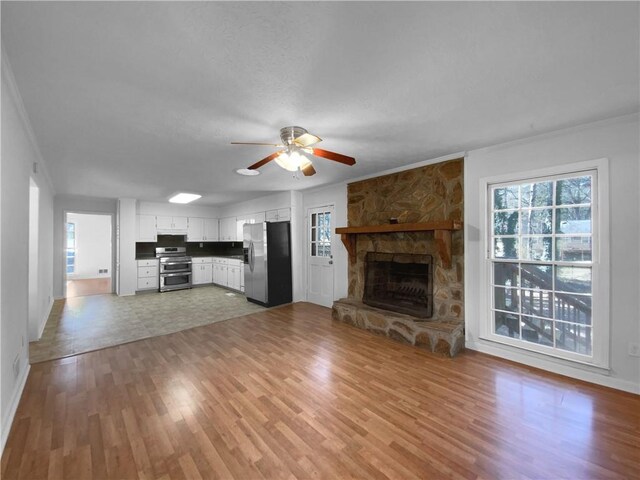8005 Bamby Ln, Jonesboro, GA 30236 - unfurnished living room featuring light wood finished floors, ceiling fan, crown molding, and a stone fireplace