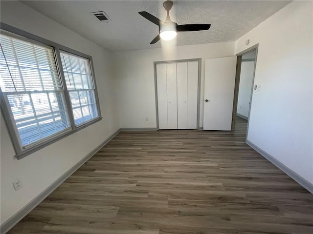 unfurnished bedroom featuring ceiling fan, a closet, dark hardwood / wood-style floors, and a textured ceiling