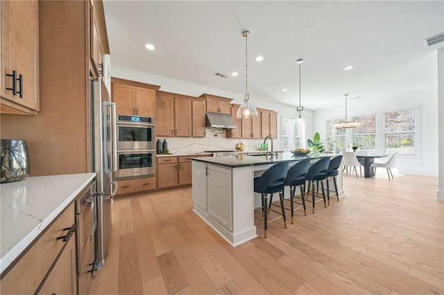 kitchen with pendant lighting, light wood-type flooring, stainless steel appliances, and a center island with sink