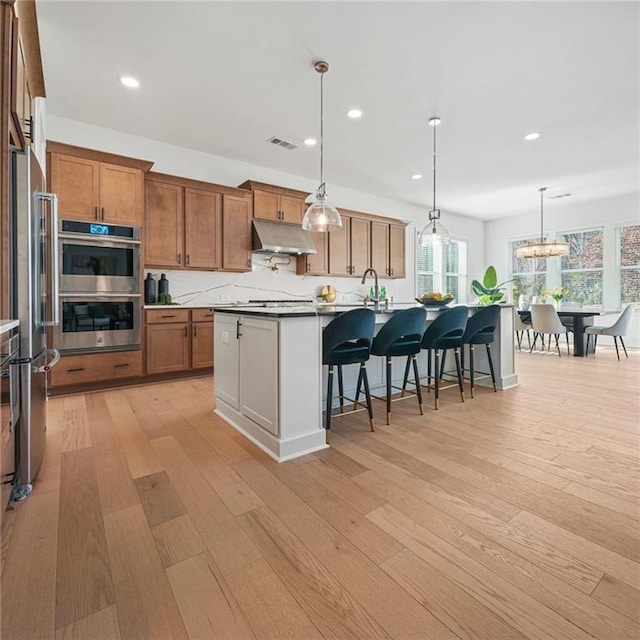 kitchen featuring visible vents, appliances with stainless steel finishes, a kitchen breakfast bar, light wood-type flooring, and under cabinet range hood