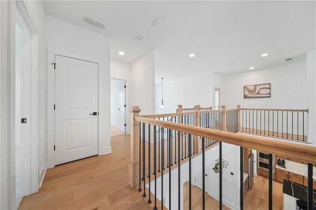 corridor with visible vents, light wood-type flooring, an upstairs landing, and recessed lighting