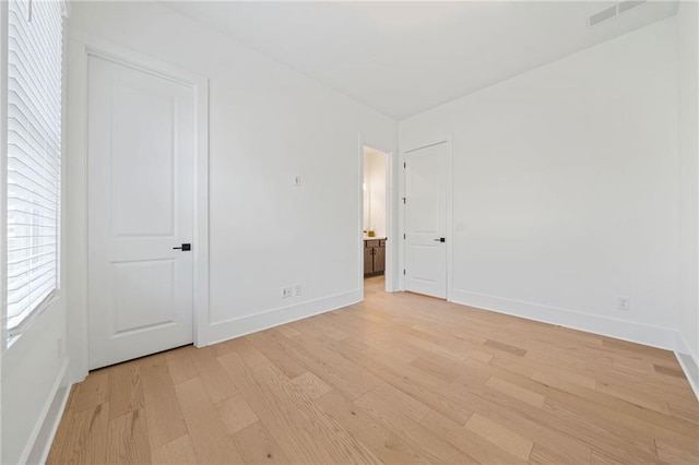 unfurnished bedroom featuring ensuite bathroom, light wood-type flooring, visible vents, and baseboards