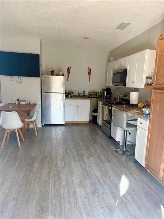 kitchen with white cabinetry, appliances with stainless steel finishes, a textured ceiling, and light hardwood / wood-style flooring