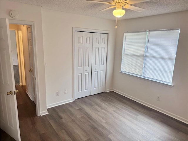 unfurnished bedroom featuring baseboards, a closet, a textured ceiling, a ceiling fan, and dark wood-style flooring