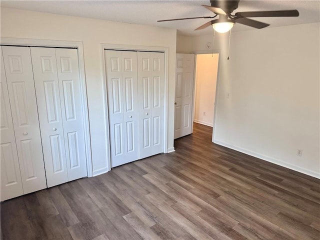 unfurnished bedroom with baseboards, multiple closets, wood finished floors, and a ceiling fan