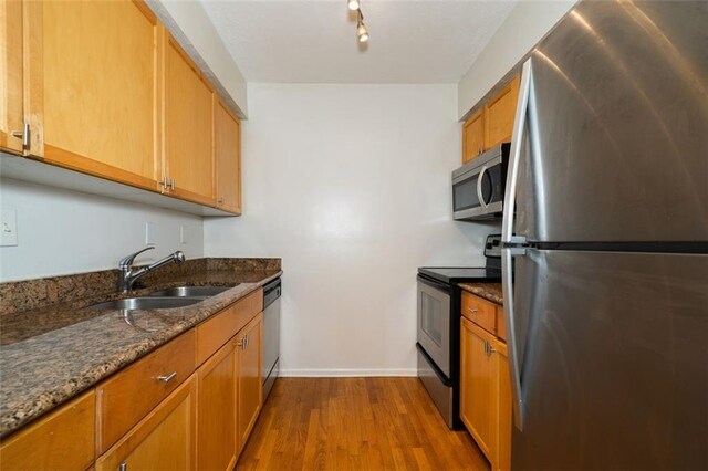 kitchen with stainless steel appliances, hardwood / wood-style flooring, dark stone countertops, rail lighting, and sink