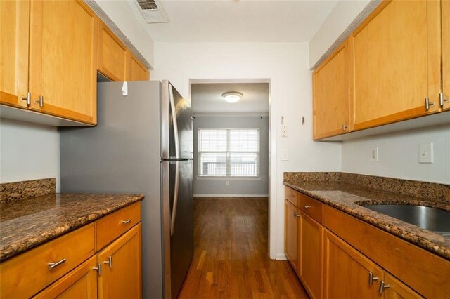 kitchen with dark stone countertops, dark hardwood / wood-style floors, and stainless steel fridge