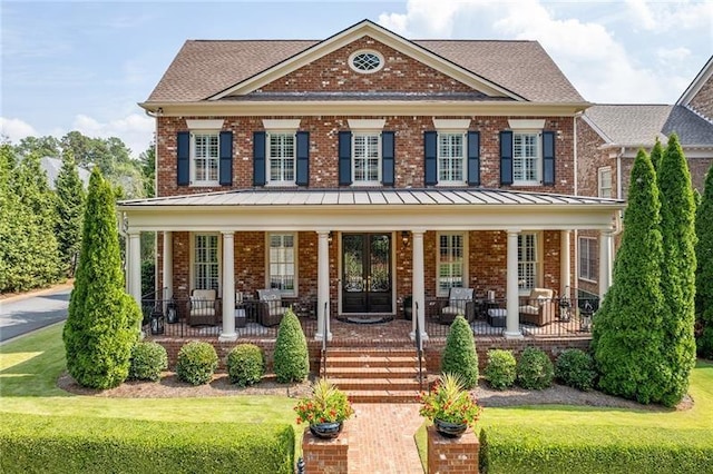 colonial house featuring covered porch, brick siding, and a standing seam roof