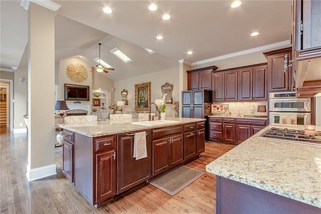 kitchen featuring light stone counters, crown molding, stainless steel appliances, a sink, and an island with sink