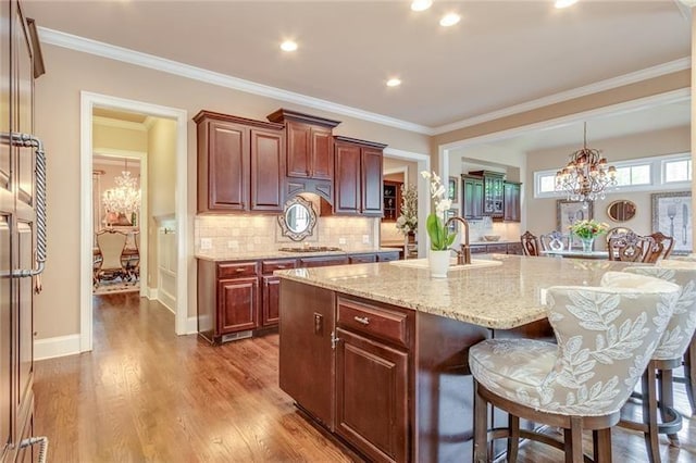 kitchen featuring decorative backsplash, a breakfast bar area, wood finished floors, a large island with sink, and a chandelier