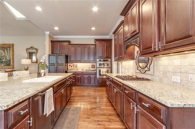 kitchen with light wood-style flooring, light stone counters, stainless steel appliances, and a sink