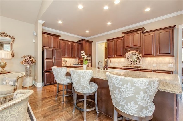 kitchen with dark wood finished floors, crown molding, a large island with sink, a kitchen bar, and a sink