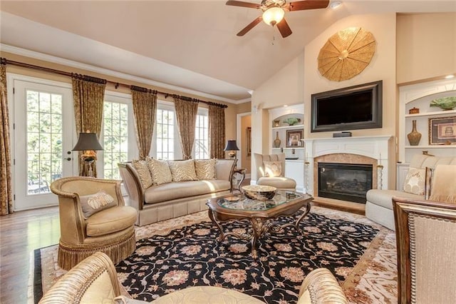 living area with built in features, ceiling fan, wood finished floors, crown molding, and a fireplace