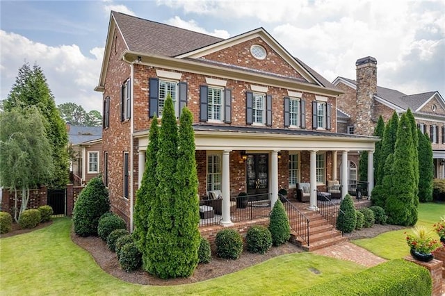 colonial-style house featuring a porch, a front lawn, a chimney, and brick siding