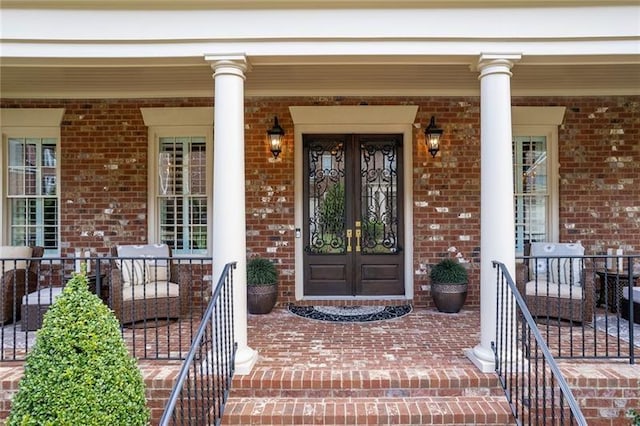 entrance to property with covered porch, french doors, and brick siding