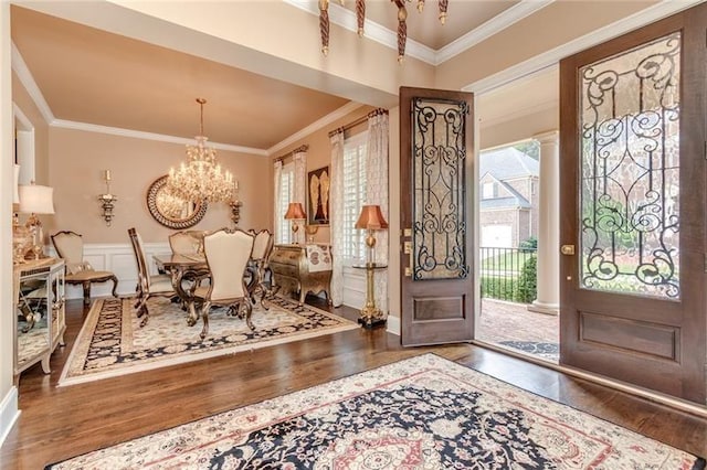 entryway featuring a decorative wall, wainscoting, an inviting chandelier, dark wood finished floors, and crown molding