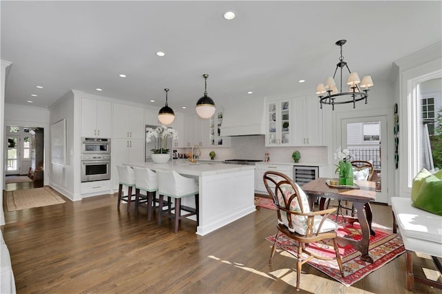 kitchen featuring white cabinetry, stainless steel appliances, custom range hood, and a center island with sink