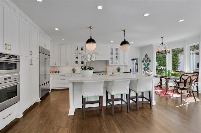 kitchen with white cabinetry, decorative light fixtures, a kitchen island with sink, and stainless steel appliances