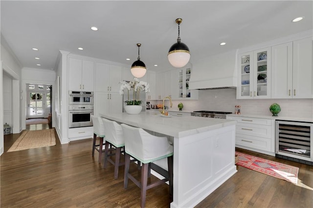 kitchen with wine cooler, custom exhaust hood, white cabinetry, double oven, and a kitchen island with sink