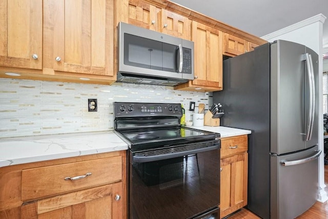 kitchen with backsplash, light stone countertops, appliances with stainless steel finishes, and light wood-style flooring