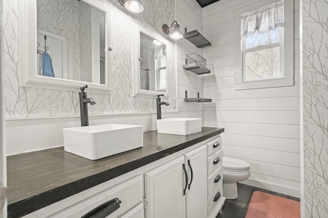 full bath with a sink, toilet, double vanity, and wood finished floors