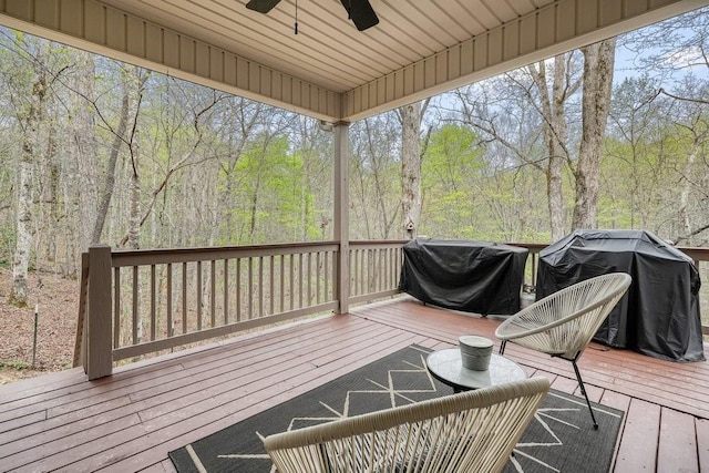 wooden terrace with a ceiling fan, a view of trees, and grilling area