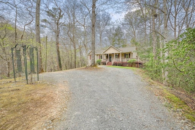 view of front of property with a view of trees, a porch, and gravel driveway